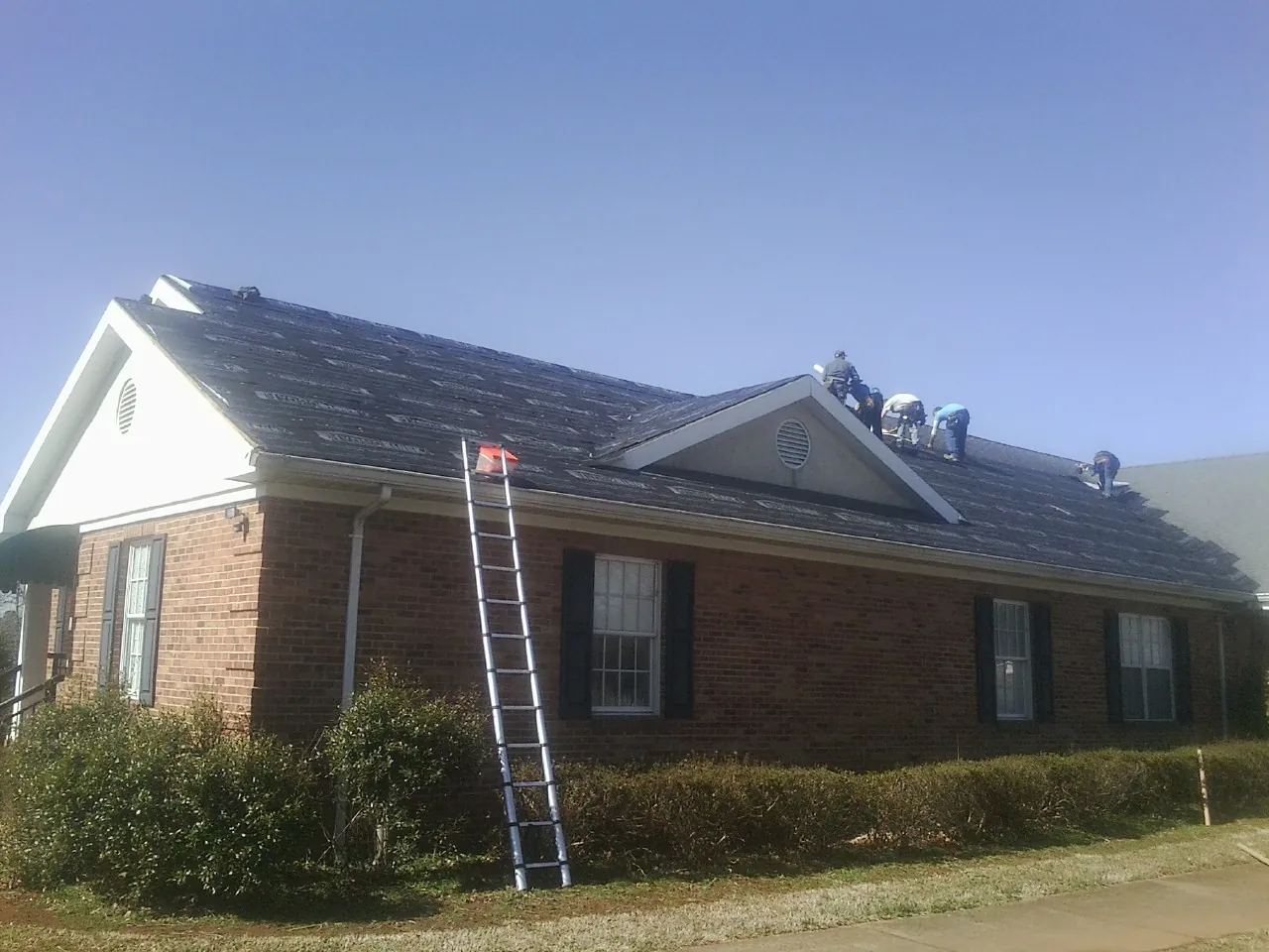 Crew tearing shingles off a brick ranch roof with a ladder set — Emergency Roof Repair work by our crew in Dorr