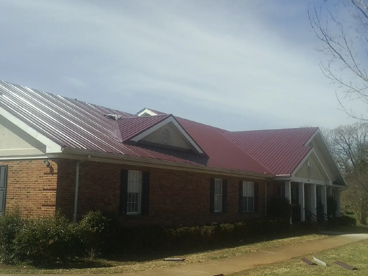 Red metal roof with gabled entries on a long brick building, from a Hail Damage Roof Repair job in Dorr