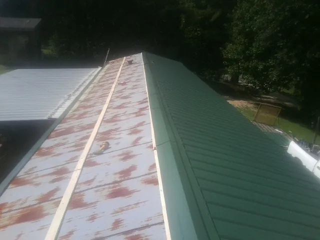 Old rusted panels beside newly installed green metal roofing — Wind Damage Roof Repair by Roofing Brothers in Dorr
