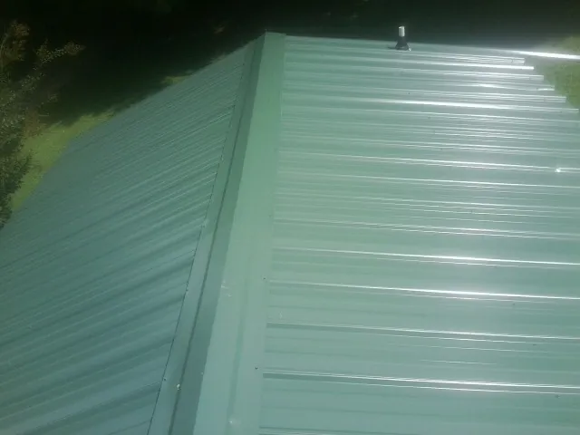 New green metal panels meeting at the ridge of a roof — Flat Roof Repair work by our crew in Dorr