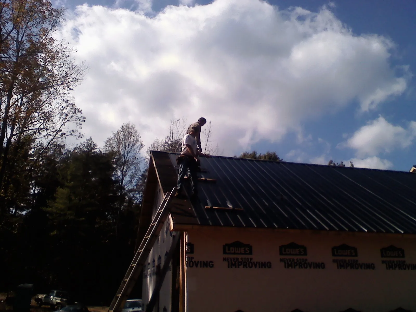 Roofer fastening dark metal panels high against a cloudy sky, from a Roof Inspection job in Dorr