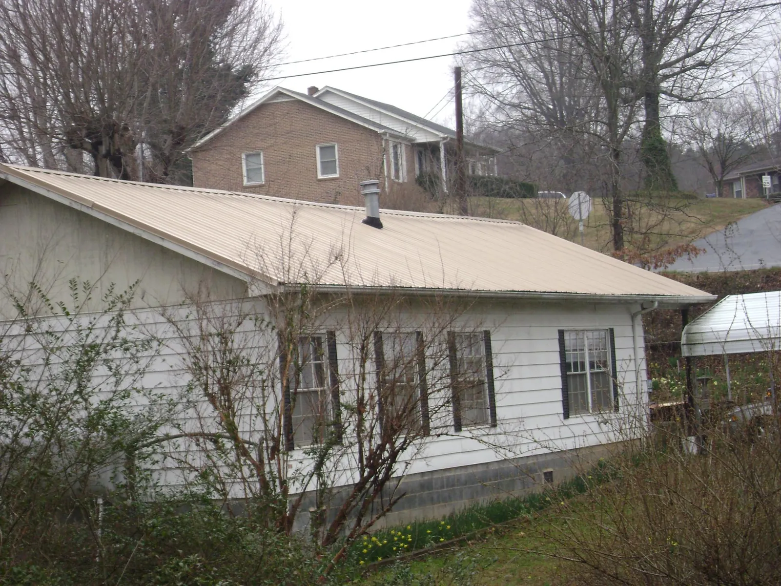 Tan metal roof on a white sided house set into a hillside — Commercial Roofing by Roofing Brothers in Dorr